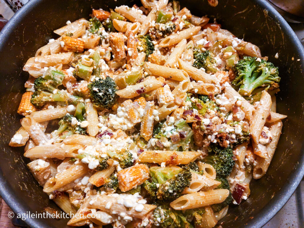 A pasta dish with broccoli, mini corn and cottage cheese cooking on the stove