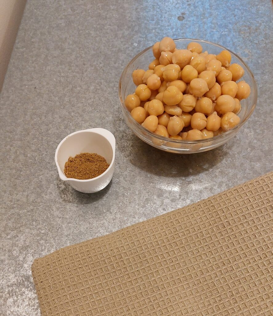 A glass bowl filled with chickpeas and a white bowl with ground cumin. 