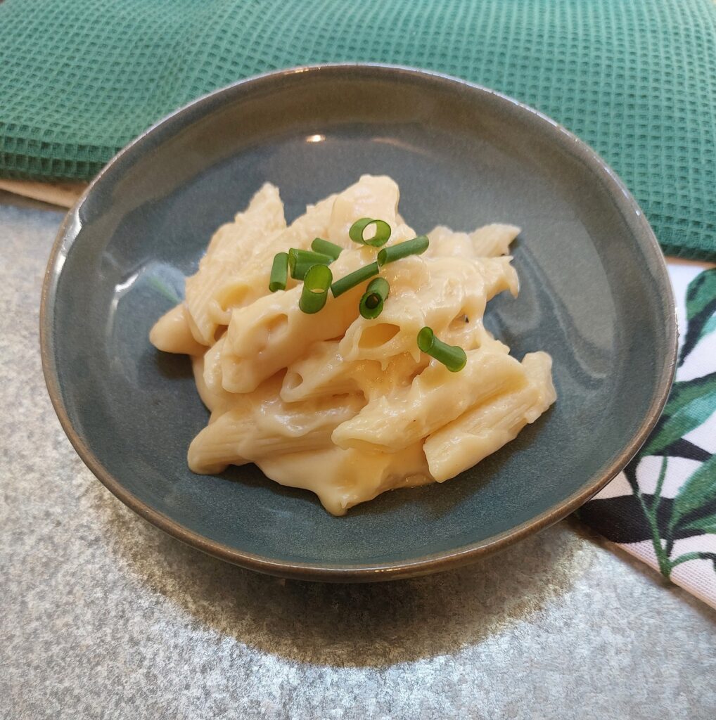 Classic Mac n Cheese placed on a blue plate and sprinkled with some green onions. The plate is placed on a green table cloth.