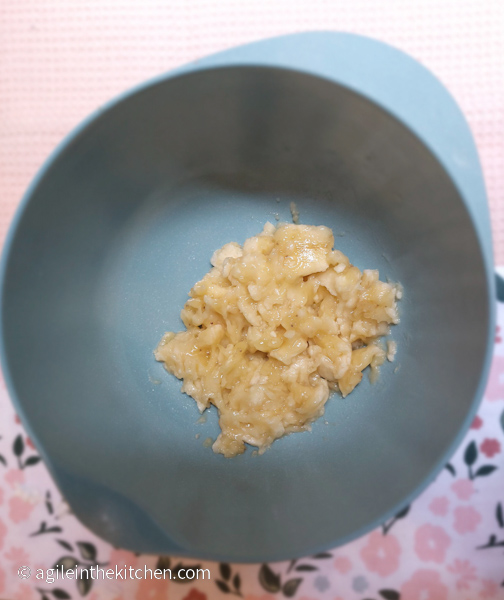 Mushed up banana in a blue bowl sitting on top of a pink and flowery table cloth