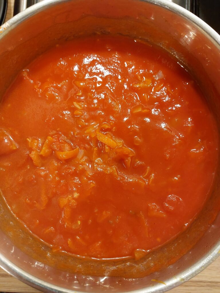 Red tomato soup simmering in a silver pot, with some shredded carrots visible.