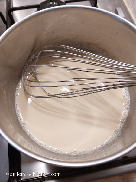 Cheese sauce cooking on the stove with a whisk in a silver coloured pot.