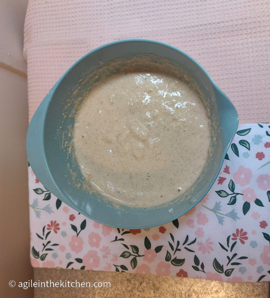 Waffle batter in a blue bowl, sitting on a pink and flowery table cloth.