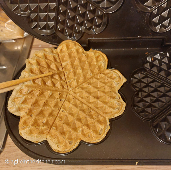 Waffle is lifted from the waffle maker using wooden chopsticks.