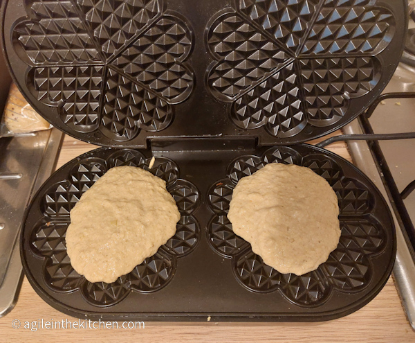 Two puddles of waffle batter are poured onto waffle maker ready to be cooked.