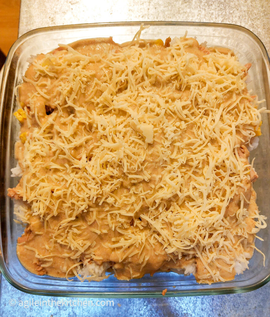 Creamy Tuna Bake in a square oven safe glass ware pan, topped with shredded cheese ready to go in to the oven