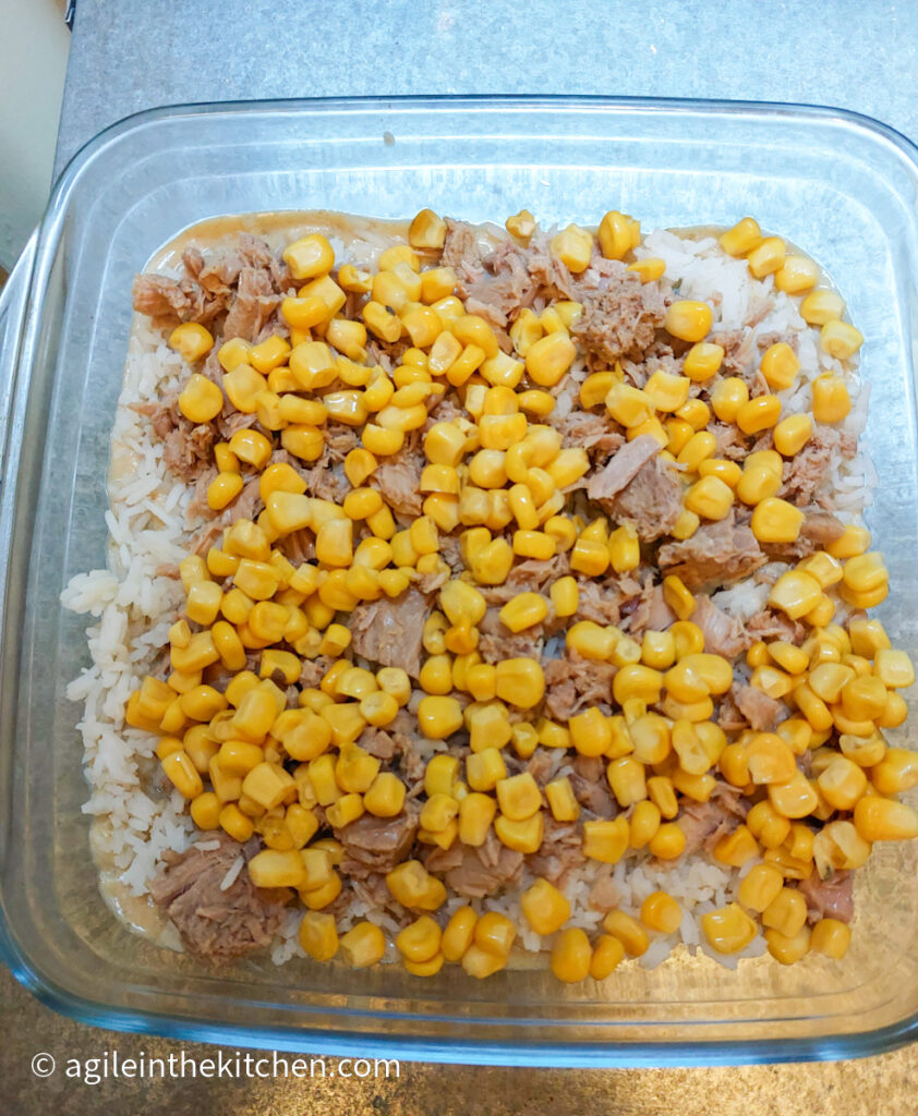 Layering a Creamy Tuna Bake with Béchamel sauce, white rice, tuna in chunks and corn