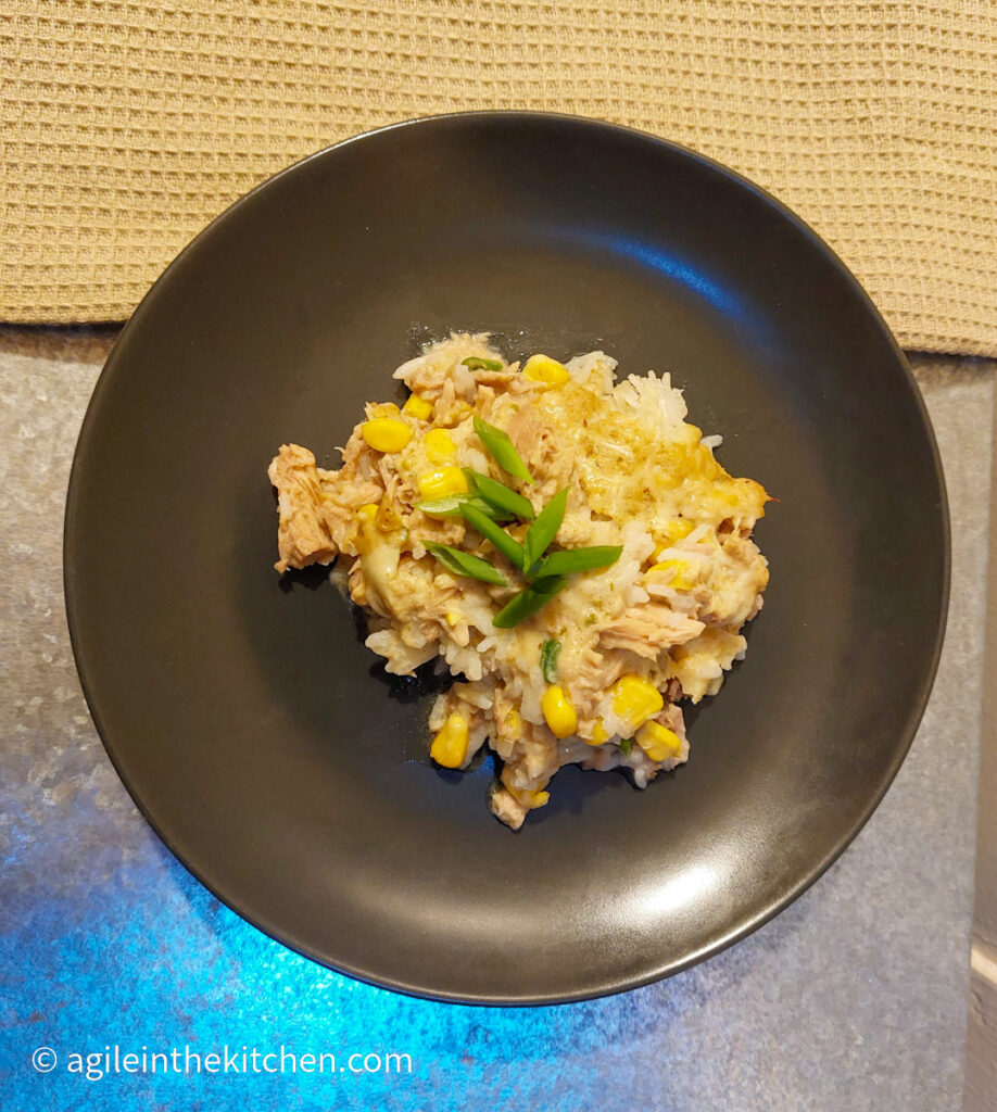 Creamy tuna bake plated on a black plate, topped with cut green onions.