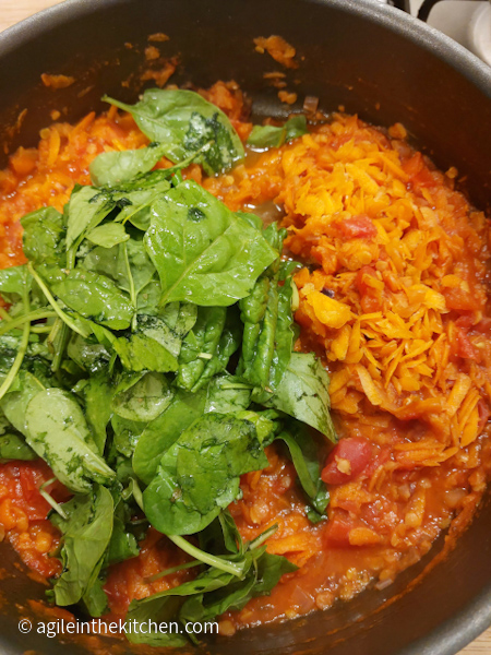 Spinach and shredded carrots added into a pot of tomato sauce, ready to stir.