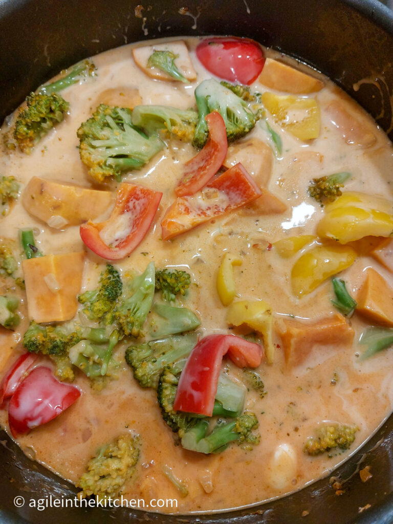 Sweet potato curry cooking in a large sauteuse, with sweet potatoes, red and yellow peppers, green broccoli in a red curry sauce