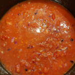 Tomato sauce cooking in a pot with red onions and red lentils.
