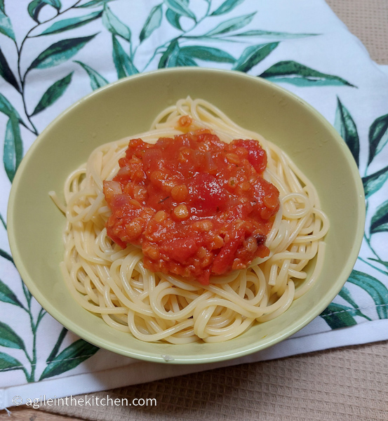 Tomato sauce plated on top of a green bowl with spaghetti that is sitting on a kitchen towel printed with green leaves. 