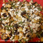 Roasted aubergine mix ready to bake in the oven with diced aubergine, diced potatoes, cut up green beans and crumbled feta cheese on a red silicone baking sheet.