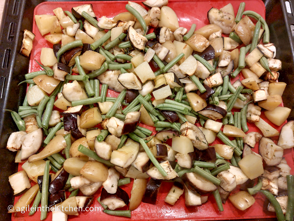 Second layer of roasted aubergine mix ready to bake in the oven with diced aubergine, diced potatoes and cut up green beans on a red silicone baking sheet