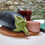 An aubergine, a glass of red ale and a pot of salt and a green napkin, resting on a cork cutting board