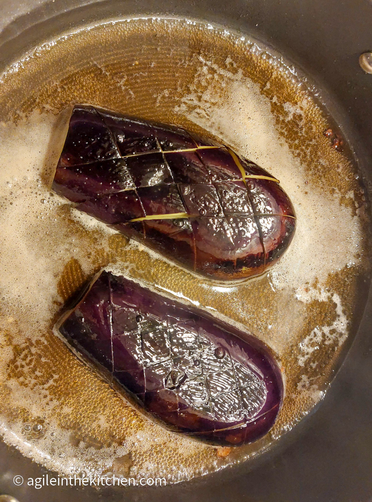 A cut and scored aubergine is cooking in a sauteuse with red ale, meaty side down