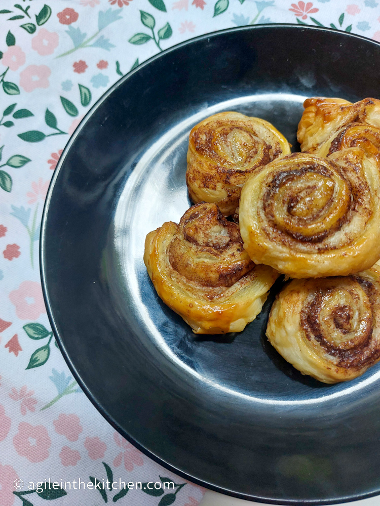 Cinnamon swirls laid on top of each other on a black plate on a background of flowery tablecloth.