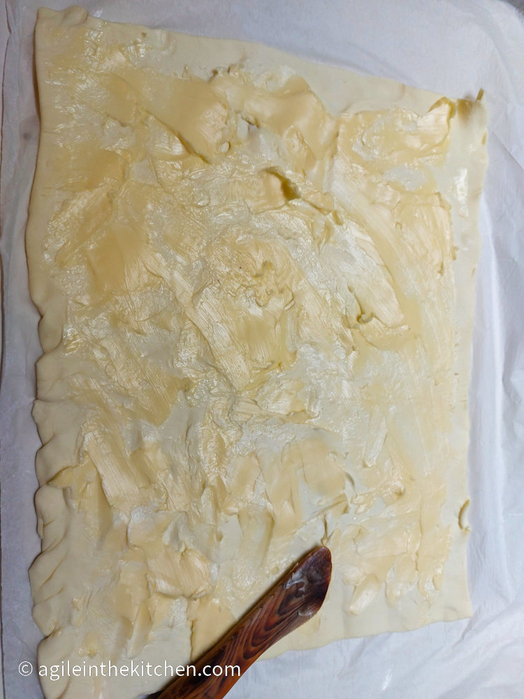 Puff pastry rolled out, smeared with butter, using a butter knife.