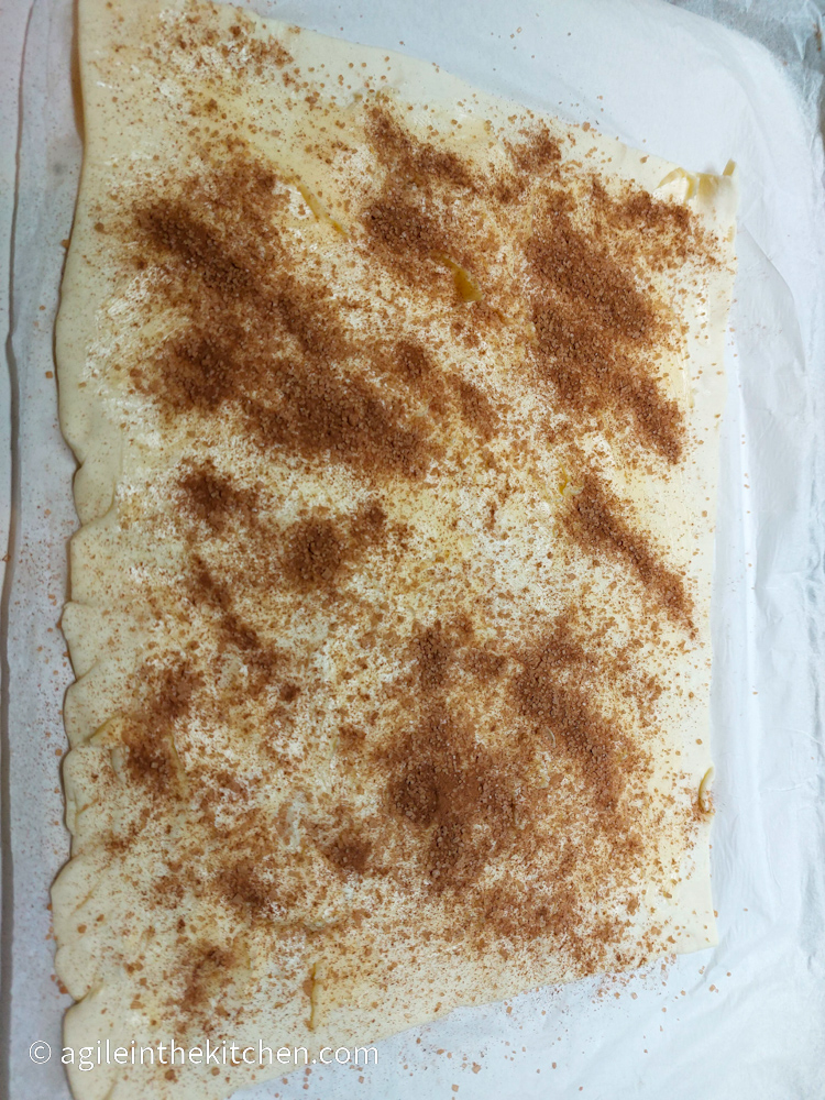 Rolled out puff pastry smeared with butter and covered with a sugar and cinnamon mix.