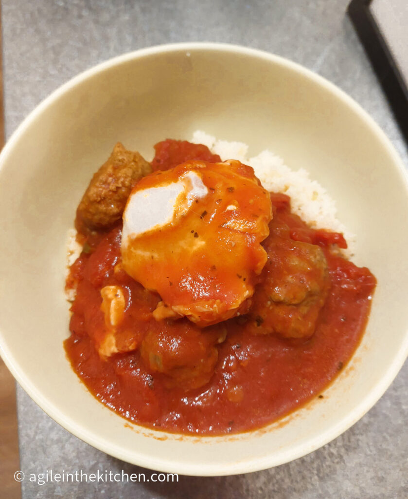 Shakshuka which is Moroccan meatballs in a red sauce and a poached egg is plated in a green bowl on top of couscous.