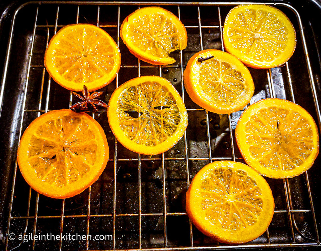 Eight saffron candied orange slices drying on a wire rack after cooking.