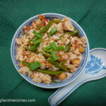 Cooked stir fry in a bowl, next to a ceramic spoon laying on top of a green table cloth