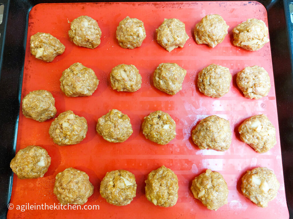 Twenty-three Moroccan meatballs rolled out, placed on a red silicone cookie sheet and ready to go in to the oven