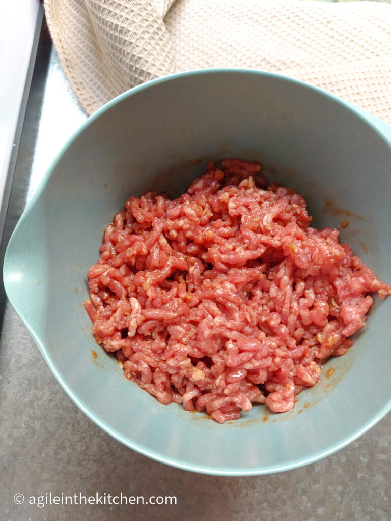 Mince meat in a blue bowl next to a beige table cloth