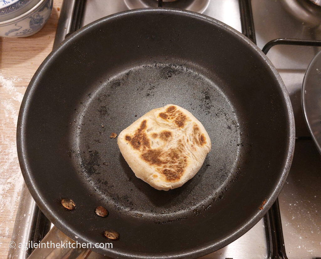 One Asian mince bun in a black frying pan, already cooked on one side, giving it a brown colouring.