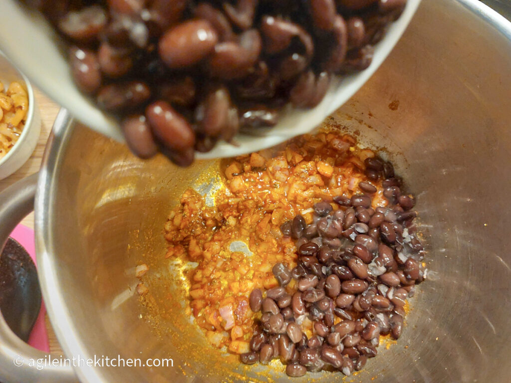 Black beans are added into a pot with onions, cumin and chili powder.