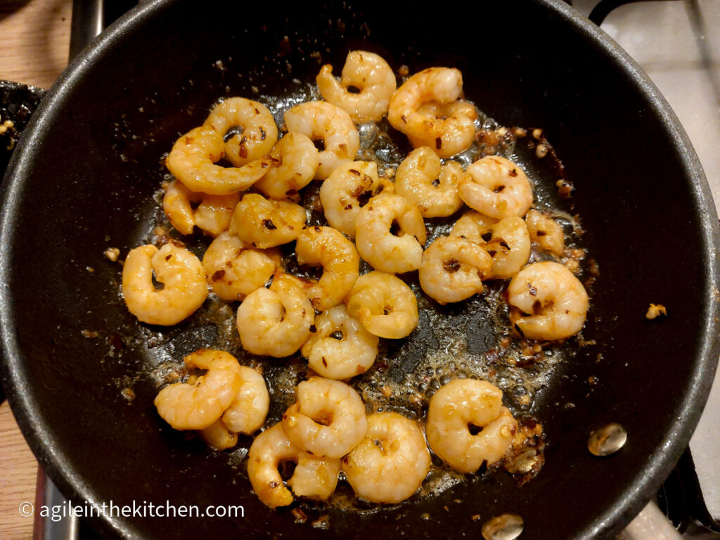 Shrimp frying in oil and chili in a black frying pan on a gas hob.