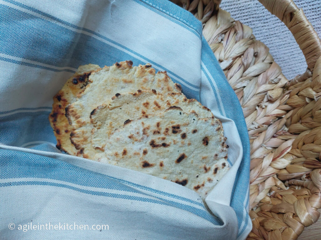 Four flat bread, covered with a white and blue cloth, placed in a wicker basket.