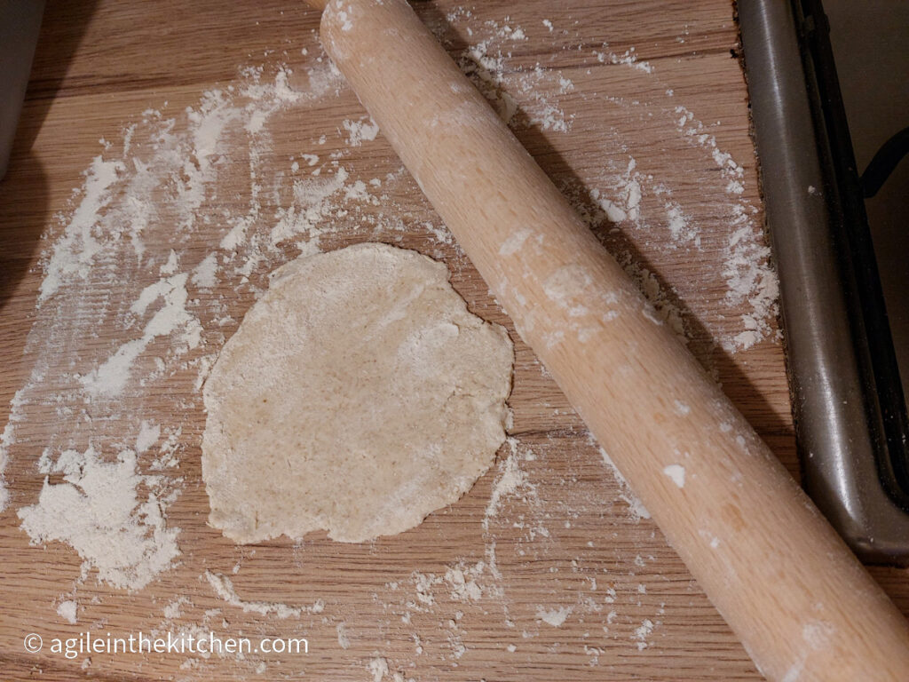 Flatbread rolled out on a table covered in flour next to a wooden rolling pin covered in flour