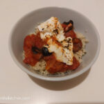 A white bowl with couscous and feta cheese bake, tomato sauce and black olives