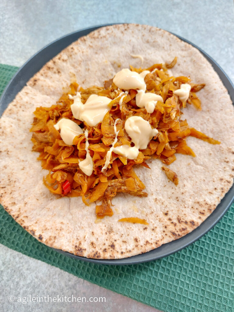 On a silver background with a green table cloth, an Asian chicken wrap on a plate made with shredded chicken and dressing on top.