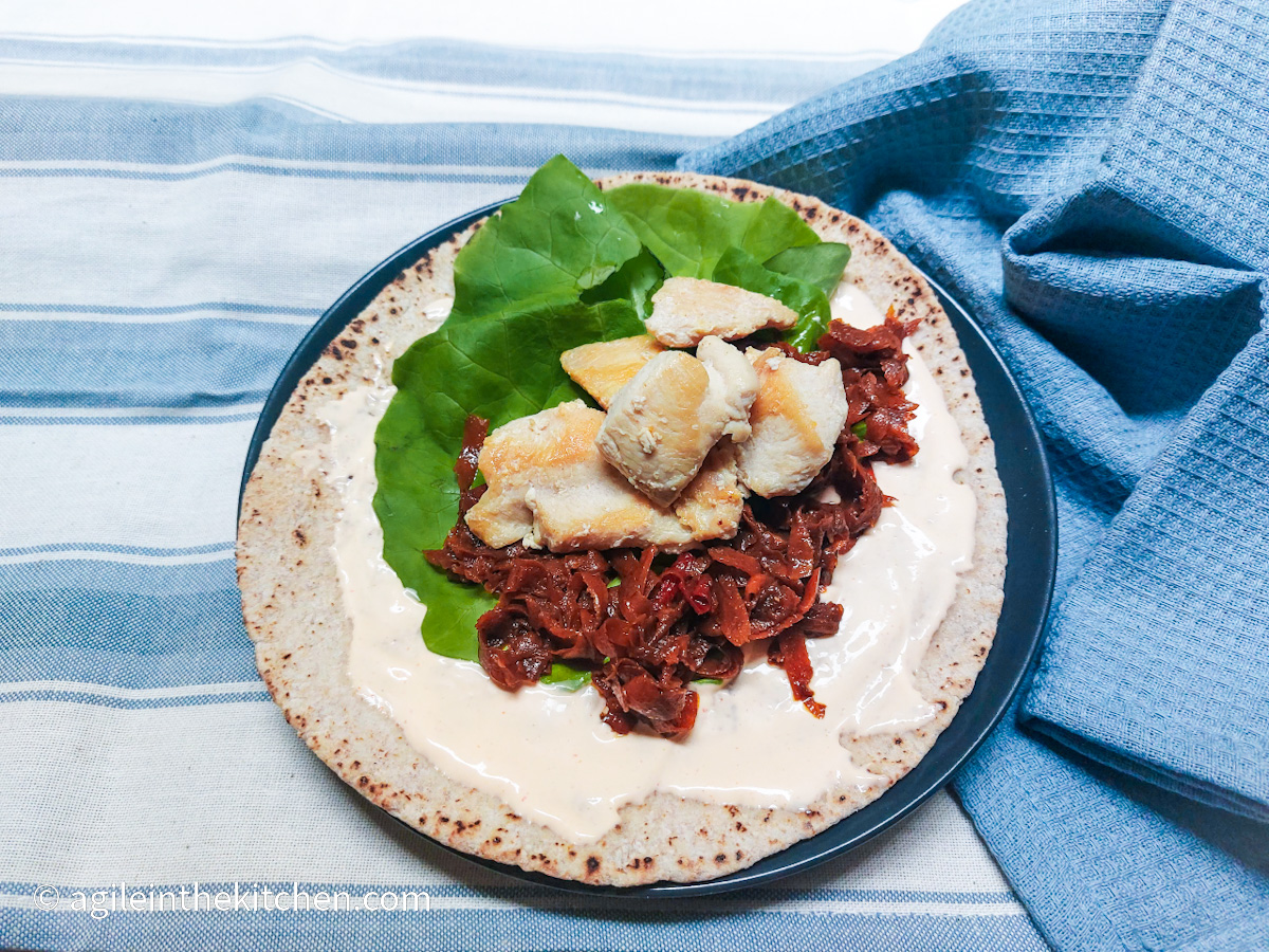 On a blue and white horizontal striped background, a plate with an Asian chicken wrap with green lettuce and diced chicken and a blue napkin crumbled up.