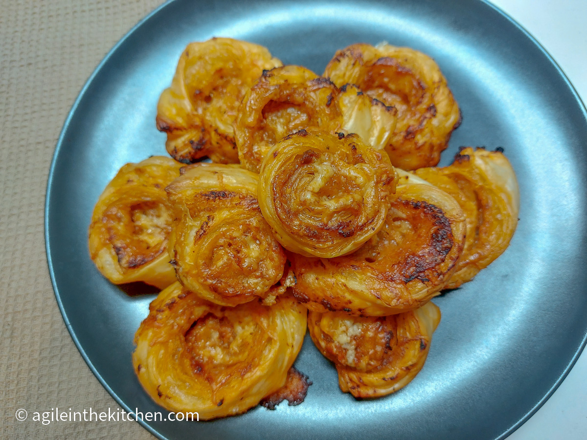 On a beige table cloth, a matte black plate, a pile of red pesto pinwheels straight from the oven.