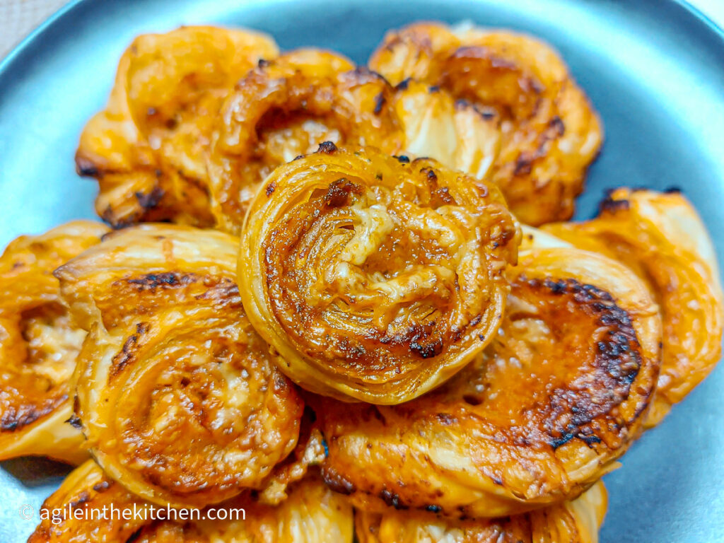 Close up of puff pastry pinwheels with red pesto from the oven, piled up on a matte black plate