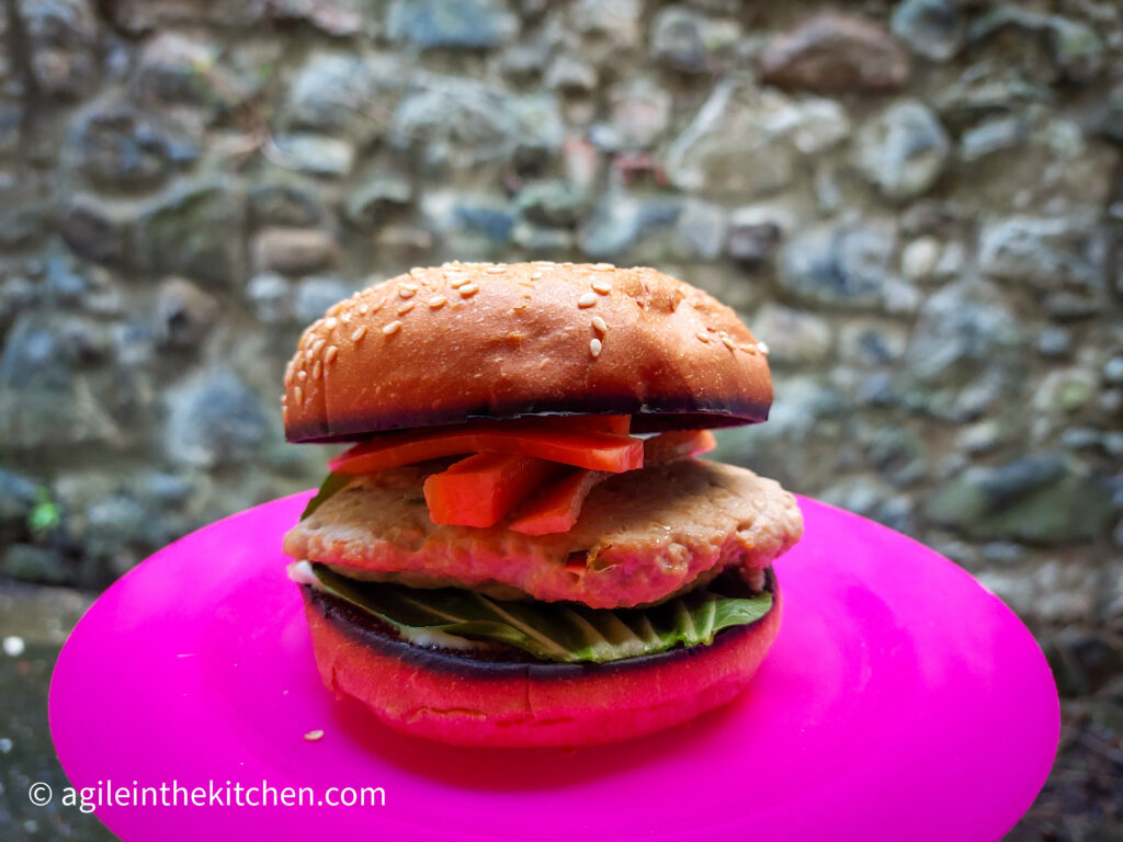 A pink plastic pick nick plate with a hamburger where pak choi, patty and pickled carrots are visible.