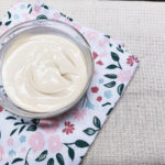 On a white table cloth, a folded cloth napkin with a flower and leaf pattern, a glass bowl with creamy mustard dressing.