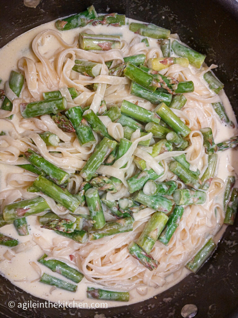 Tagliatelle is mixed in a wide pot together with cut, green asparagus and a white sauce