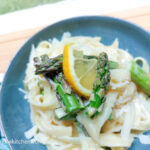 A blue plate with lemon asparagus pasta laid out. In focus is a few pieces of cut asparagus and a quarter slice of lemon.