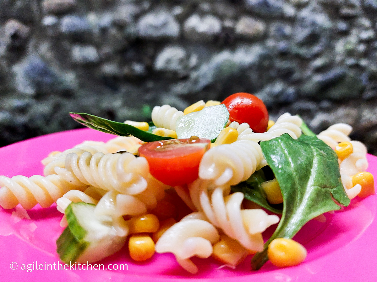 On a pink plate, a close up of a basic pasta salad