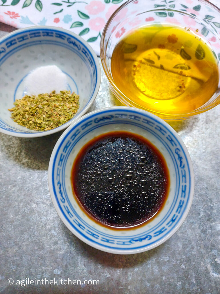 Three bowls with ingredients to make a salad dressing; balsamic vinegar, olive oil, salt and oregano