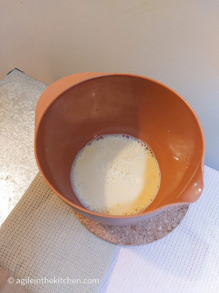 On a textured background, an orange bowl with eggs beaten