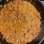 In a frying pan, taco mince meat cooking together, with mince meat, red split lentils and taco seasoning