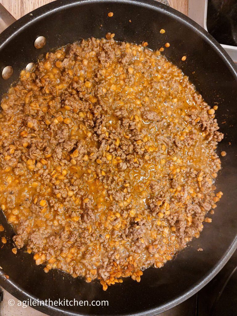 In a frying pan, taco mince meat cooking together, with mince meat, red split lentils and taco seasoning