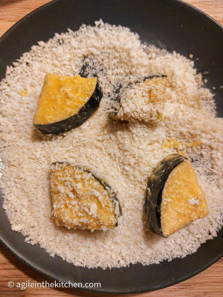 On a black plate, five aubergine bites covered in egg and resting in panko bread crumbs