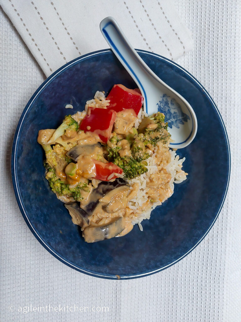 On a white textured background, a blue bowl on a bed of rice, vegetable red curry