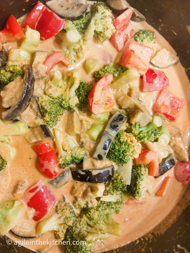 In a pot, vegetable red curry, in the photo can be seen aubergine, broccoli, and red pepper.